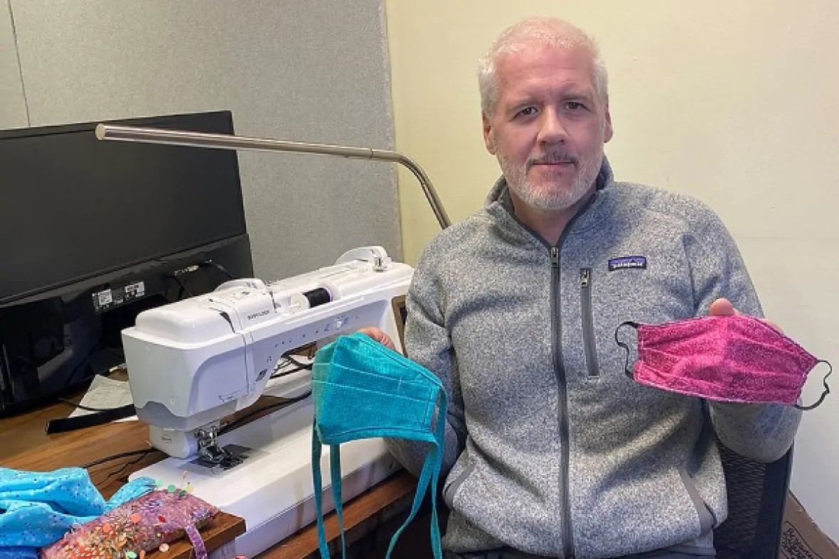 Ken Drouillard holds up two facemasks in front of a sewing machine